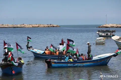 Palestinians hold flags as they ride a boat during a protest to break the siege, at the seaport of Gaza City May 30, 2016. Photo by Mohammed Asad