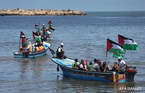 Palestinians hold flags as they ride a boat during a protest to break the siege, at the seaport of Gaza City May 30, 2016. Photo by Mohammed Asad