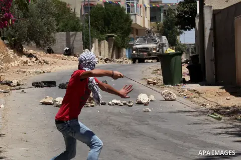 A Palestinian protester uses a slingshot to throw stones towards Israeli security forces during clashes following a demonstration against the expropriation of Palestinian land by Israel, on June 10, 2016. in the village...