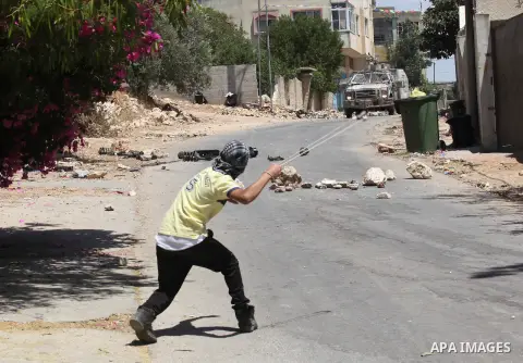 A Palestinian protester uses a slingshot to throw stones towards Israeli security forces during clashes following a demonstration against the expropriation of Palestinian land by Israel, on June 10, 2016. in the village...