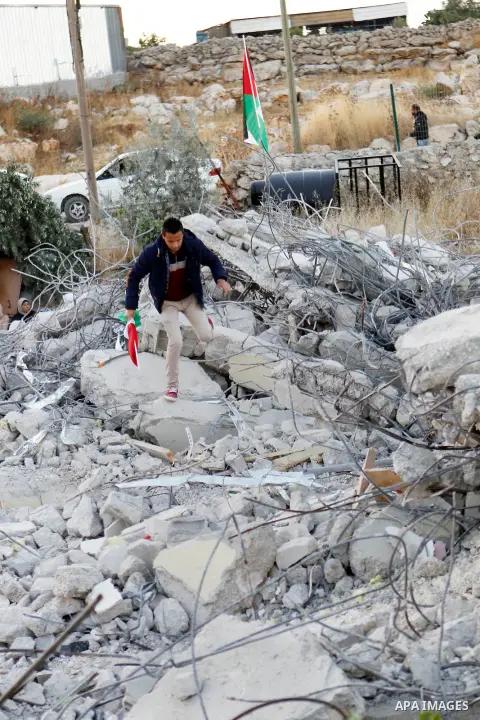 A Palestinian youth holds a Palestinian flag as he stands at the rubble of Palestinian teenager Murad Idais house who was accused of stabbing to death a 38-year old Israeli nurse in an attack in the Israeli Otniel settle...