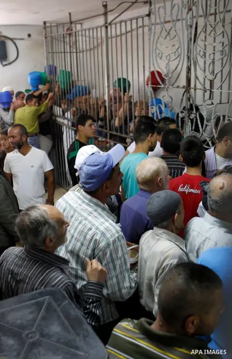 Palestinian families carry containers as they wait to receive free food for 'Iftar', the meal that breaks the daily fast during Ramadan in the West Bank city of Hebron, 13 June 2016. the "Ibrahimi Takiya" was founded in...