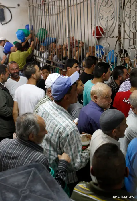 Palestinian families carry containers as they wait to receive free food for 'Iftar', the meal that breaks the daily fast during Ramadan in the West Bank city of Hebron, 13 June 2016. the "Ibrahimi Takiya" was founded in...