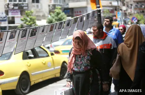 Palestinians walk past posters hanging for martyrs to show solidarity with them, in the West Bank city of Ramallah on June 13, 2016. Photo by Shadi Hatem