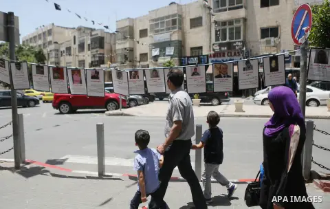 Palestinians walk past posters hanging for martyrs to show solidarity with them, in the West Bank city of Ramallah on June 13, 2016. Photo by Shadi Hatem