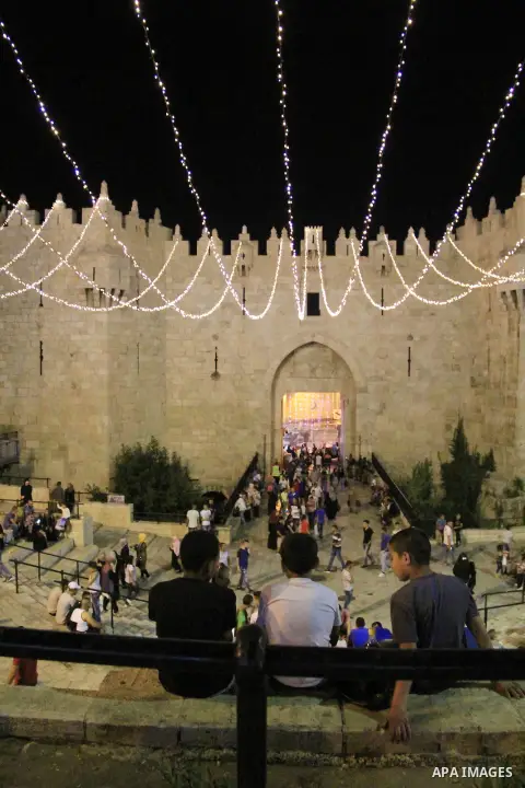 Palestinians walk under lights decorating Damascus Gate following "Taraweeh", nightly prayer of the month of Ramadan, at al-Aqsa mosque, in Jerusalem's old city on June 14, 2016. Ramadan is sacred to Muslims because it i...