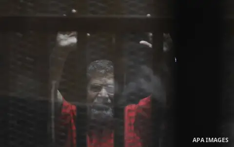 Egypt's ousted Islamist president Mohamed Morsi, wearing a red uniform, looks on from behind the defendant's bars during his trial on espionage charges at a court in Cairo on June 18, 2016. An Egyptian court sentenced Mo...