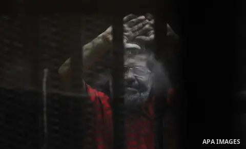 Egypt's ousted Islamist president Mohamed Morsi, wearing a red uniform, looks on from behind the defendant's bars during his trial on espionage charges at a court in Cairo on June 18, 2016. An Egyptian court sentenced Mo...