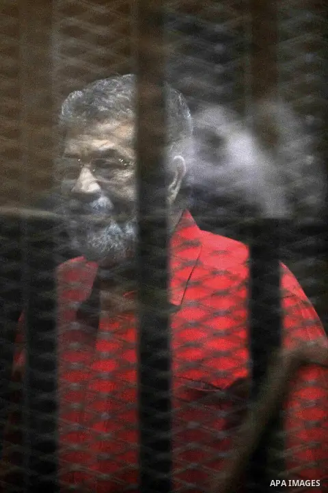 Egypt's ousted Islamist president Mohamed Morsi, wearing a red uniform, looks on from behind the defendant's bars during his trial on espionage charges at a court in Cairo on June 18, 2016. An Egyptian court sentenced Mo...