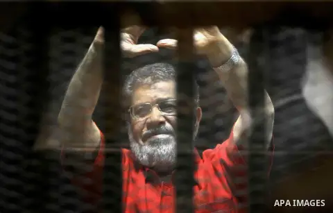 Egypt's ousted Islamist president Mohamed Morsi, wearing a red uniform, looks on from behind the defendant's bars during his trial on espionage charges at a court in Cairo on June 18, 2016. An Egyptian court sentenced Mo...