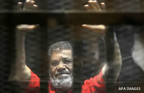 Egypt's ousted Islamist president Mohamed Morsi, wearing a red uniform, looks on from behind the defendant's bars during his trial on espionage charges at a court in Cairo on June 18, 2016. An Egyptian court sentenced Mo...