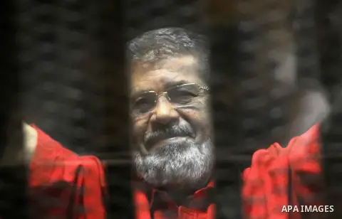 Egypt's ousted Islamist president Mohamed Morsi, wearing a red uniform, looks on from behind the defendant's bars during his trial on espionage charges at a court in Cairo on June 18, 2016. An Egyptian court sentenced Mo...