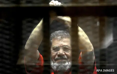 Egypt's ousted Islamist president Mohamed Morsi, wearing a red uniform, looks on from behind the defendant's bars during his trial on espionage charges at a court in Cairo on June 18, 2016. An Egyptian court sentenced Mo...