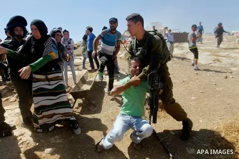 An Israeli soldier grabs a Palestinian man as Israeli troops demolish sheds belonging to Palestinians near the West Bank village of Yatta, south of Hebron June 19, 2016. Photo by Wisam Hashlamoun