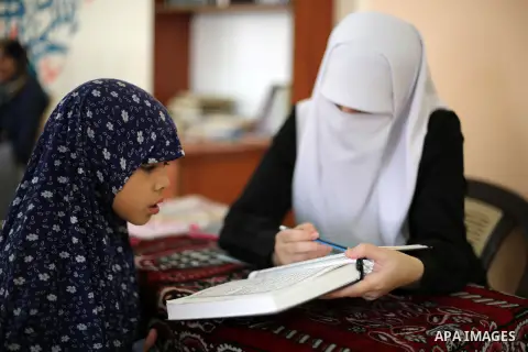 A Palestinian woman reads with a young girl from a copy of the Koran, Islam's holy book, at a religion school in Gaza City on June 21, 2016, during the Muslim fasting month of Ramadan. Photo by Mohammed Asad