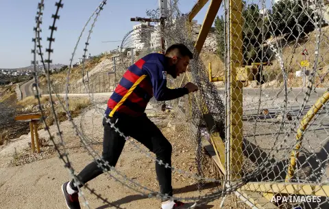 A Palestinian passes through an opening in the Israeli barrier fence as he attempts to make his way to attend the third Friday prayer of the holy fasting month of Ramadan in Jerusalem's al-Aqsa mosque, near the West bank...