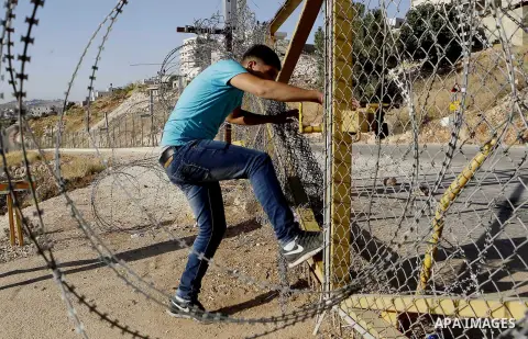 A Palestinian passes through an opening in the Israeli barrier fence as he attempts to make his way to attend the third Friday prayer of the holy fasting month of Ramadan in Jerusalem's al-Aqsa mosque, near the West bank...