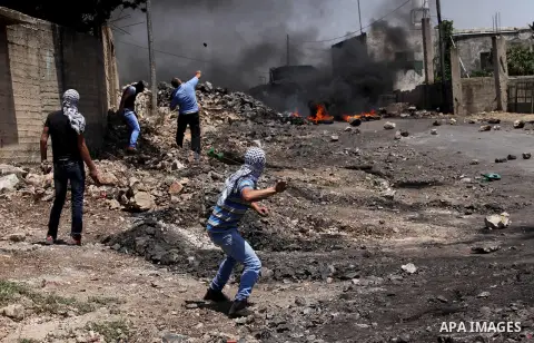 Palestinian protesters use a slingshot to hurl stones towards Israeli security forces during clashes following a demonstration against the expropriation of Palestinian land by Israel on June 24, 2016 in the village of Kf...