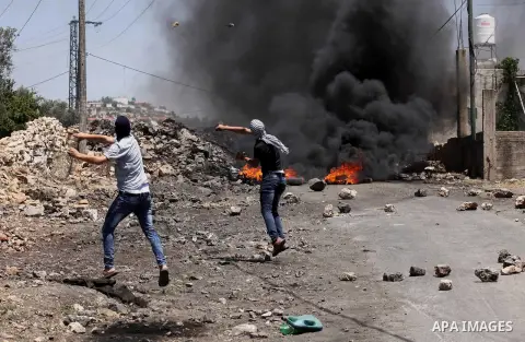 Palestinian protesters use a slingshot to hurl stones towards Israeli security forces during clashes following a demonstration against the expropriation of Palestinian land by Israel on June 24, 2016 in the village of Kf...