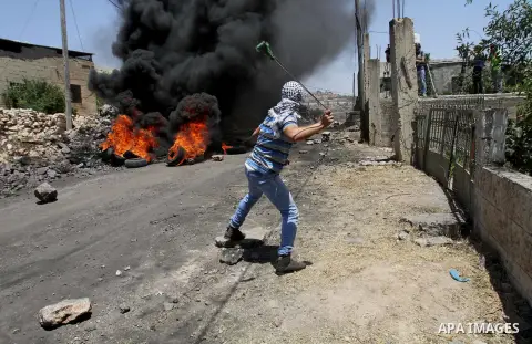A Palestinian protester uses a slingshot to hurl stones towards Israeli security forces during clashes following a demonstration against the expropriation of Palestinian land by Israel on June 24, 2016 in the village of...