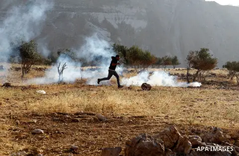 Palestinians run for a cover from teargas canisters fired by Israeli border police near a barbed-wire gate part of the controversial Israeli separation fence between the West Bank town of Bethlehem and Jerusalem, after a...