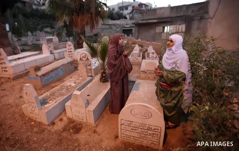 Palestinian women visit the graves of relatives at a cemetery on the first day of Eid al-Fitr celebrations, which marks the end of the holy fasting month of Ramadan, in the West Bank city of Nablus, on July 6, 2016. Phot...