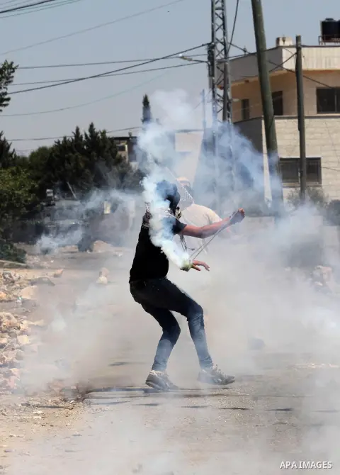 A Palestinian protester uses a slingshot to hurl back a tear gas canister fired by Israeli security forces during clashes following a demonstration against the expropriation of Palestinian land by Israel on July 15, 2016...