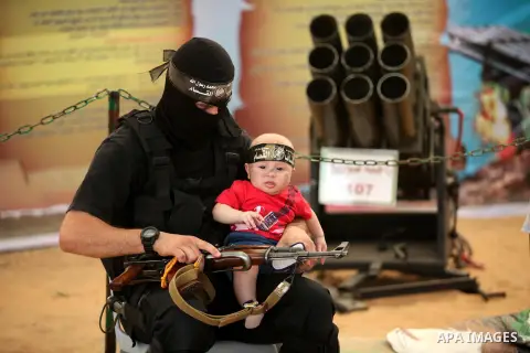 A member of the Ezzedine al-Qassam Brigades, the military wing of the Palestinian Islamist movement Hamas, carries a girl during a weapon exhibition at a Hamas-run youth summer camp, in Gaza City, on July 21, 2016. Photo...