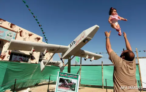 A Palestinian man palys with hid daughter next to Hamas drone "Ababil" during a weapon exhibition at a Hamas-run youth summer camp, in Gaza City, on July 21, 2016. Photo by Ashraf Amra
