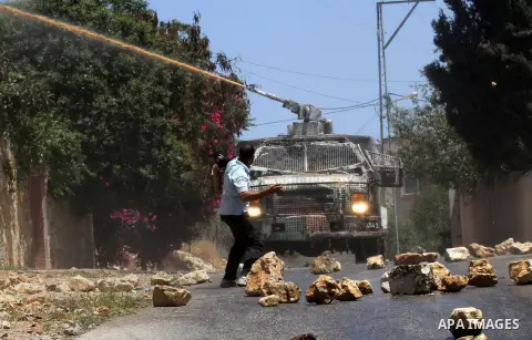A Palestinian protester throws stones towards an Israeli security forces vehicle spraying a foul-smelling water known as "skunk" during clashes following the weekly demonstration against the expropriation of Palestinian...