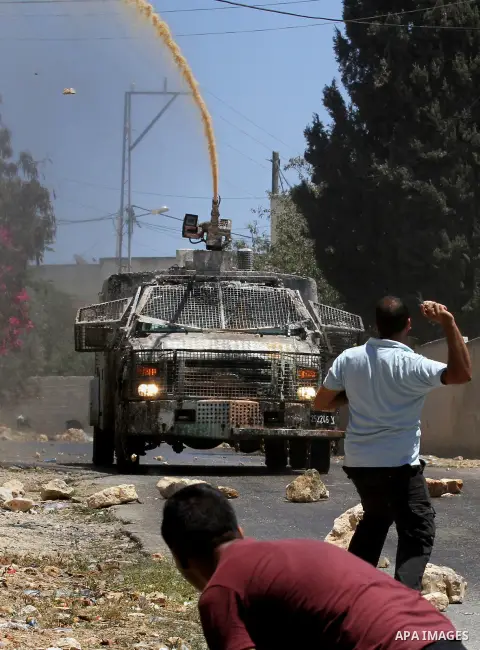 Palestinian protesters throw stones towards an Israeli security forces vehicle spraying a foul-smelling water known as "skunk" during clashes following the weekly demonstration against the expropriation of Palestinian la...