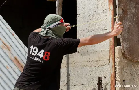 A Palestinian protestor uses a slingshot to hurl stones towards Israeli security forces during clashes following the weekly demonstration against the expropriation of Palestinian land by Israel in the village of Kfar Qad...