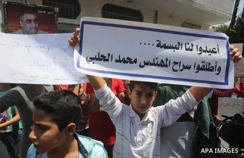 Palestinian demonstrators hold posters of Mohammad El Halabi, World Vision's manager of operations in Gaza who was accused by Israel of funnelling millions of dollars in aid money to Hamas, during a protest in solidarity...