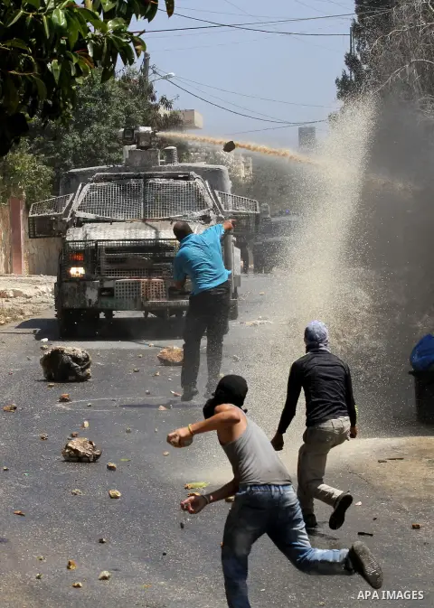 Palestinian protesters hurl stones towards an Israeli security forces vehicle spraying a foul-smelling water known as "skunk" during clashes following a weekly demonstration against the expropriation of Palestinian land...