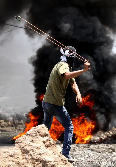 A Palestinian protester uses a slingshot to hurl stones toward Israeli security forces during clashes following a weekly demonstration against the expropriation of Palestinian land by Israel on August 12, 2016, in the vi...