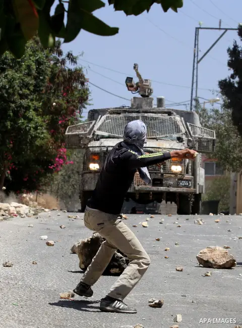 A Palestinian protester hurls stones towards an Israeli security forces vehicle spraying a foul-smelling water known as "skunk" during clashes following a weekly demonstration against the expropriation of Palestinian lan...