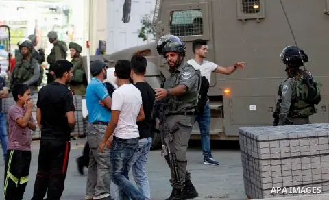 Israeli soldiers stand guard as Israeli settlers walk on a street in a Palestinian neighbourhood in the divided West Bank city of Hebron as they are heading to the Jewish shrine of Atnaeil Ben Kinaz on August 14,2016. Or...