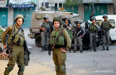 Israeli soldiers stand guard as Israeli settlers walk on a street in a Palestinian neighbourhood in the divided West Bank city of Hebron as they are heading to the Jewish shrine of Atnaeil Ben Kinaz on August 14,2016. Or...