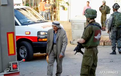 A Palestinian man walks in front of an Israeli soldier at a street in a Palestinian neighbourhood in the divided West Bank city of Hebron as Israeli settlers are heading to the Jewish shrine of Atnaeil Ben Kinaz on Augus...