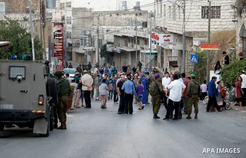 Israeli soldiers stand guard as Israeli settlers walk on a street in a Palestinian neighbourhood in the divided West Bank city of Hebron as they are heading to the Jewish shrine of Atnaeil Ben Kinaz on August 14,2016. Or...