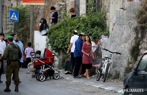 An Israeli soldier stands guard as Israeli settlers walk on a street in a Palestinian neighbourhood in the divided West Bank city of Hebron as they are heading to the Jewish shrine of Atnaeil Ben Kinaz on August 14,2016....