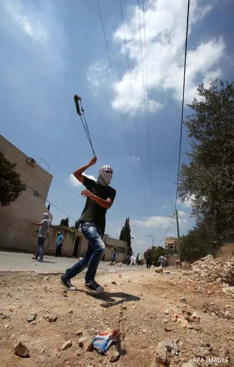 A Palestinian protester uses a slingshot to hurl stones towards Israeli security forces during clashes following a weekly demonstration against the expropriation of Palestinian land by Israel on August 19, 2016, in the v...