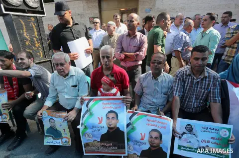 Palestinians hold posters against administrative detention and in support of Palestinian prisoner Bilal Kayed (portrait), who has been fasting for almost two months over his detention without trial, in front of Red Cross...