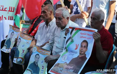 Palestinians hold posters against administrative detention and in support of Palestinian prisoner Bilal Kayed (portrait), who has been fasting for almost two months over his detention without trial, in front of Red Cross...