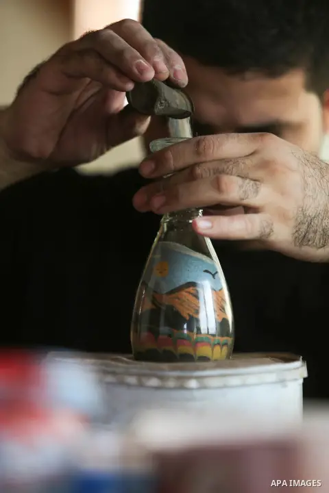 A Palestinian artist Khaled Salama, 27, paints on glass pots using colored sand, at his work shop in the West Bank city of Salfit, on Sep. 27, 2016. Photo by Shadi Hatem
