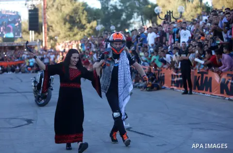 A Palestinian woman wearing a traditional dress greets stunt rider Rok Bagoros as he wears the Palestinian keffiyeh during a show in the West Bank city of Ramallah September 30, 2016. Photo by Shadi Hatem