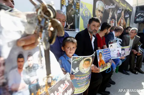 Palestinians hold banners during a protest to show solidarity with Palestinian prisoners in Israeli jails, in front of Red cross office in the West Bank city of Hebron, on October 31, 2016. Photo by Wisam Hashlamoun