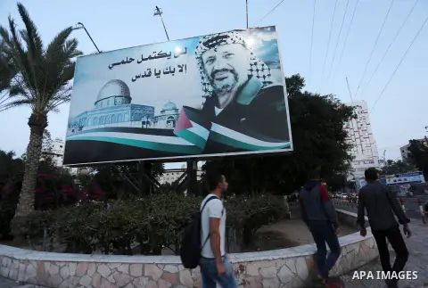 Palestinians walk in front of a poster of the late Palestinian leader Yasser Arafat, on the 12 anniversary of his death in Gaza city on Nov. 11, 2016. Photo by Mohammed Asad
