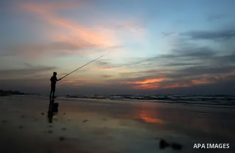A Palestinian man uses a hook to fishing off the beach of Gaza City on November 14, 2016. Photo by Yasser Qudih