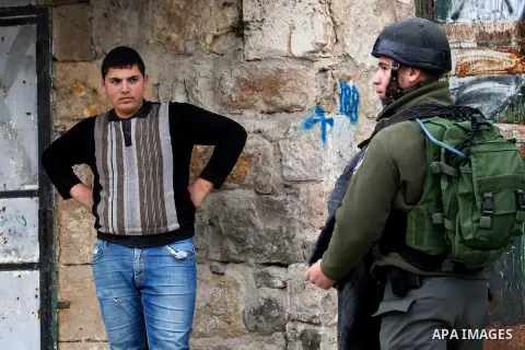 An Israeli soldier checks a Palestinian man at a checkpoint in the West Bank city of Hebron, on Nov. 22, 2016. Photo by Wisam Hashlamoun